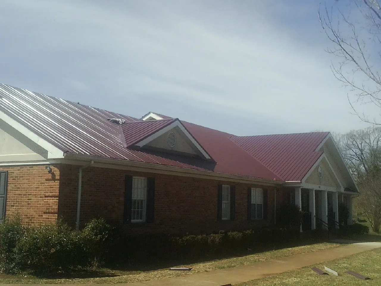 Red metal roof with gabled entries on a long brick building, from a Hail Damage Roof Repair job in Weatherford