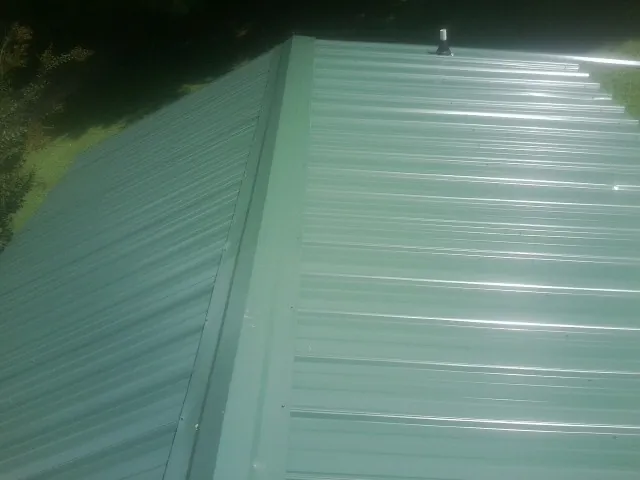 New green metal panels meeting at the ridge of a roof — Flat Roof Repair work by our crew in Weatherford