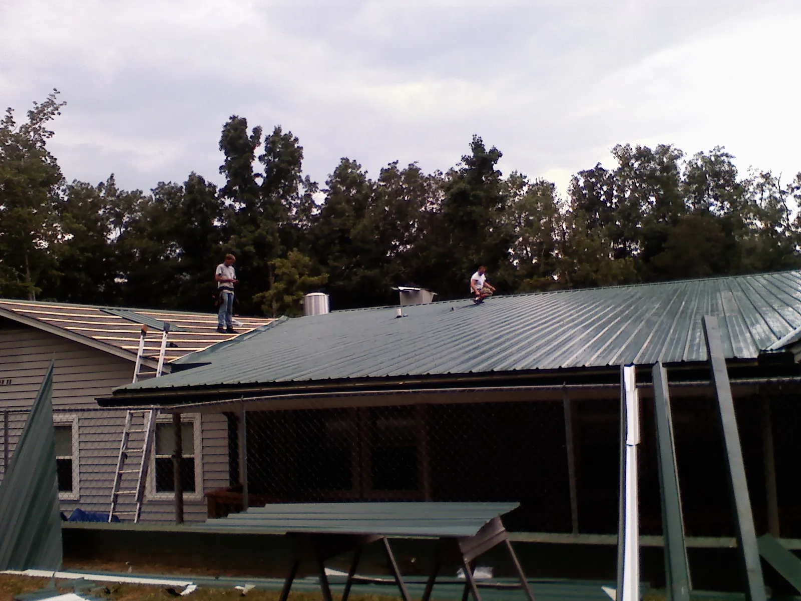 Two roofers installing green metal panels above a covered porch in Weatherford