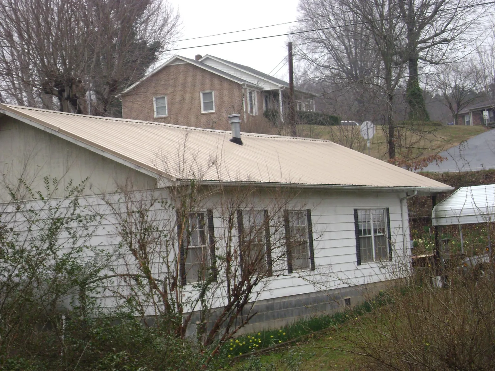 Tan metal roof on a white sided house set into a hillside — Commercial Roofing by Roofing Brothers in Weatherford